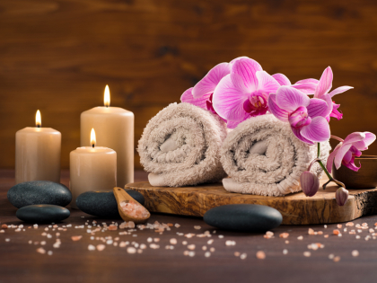 Spa setting with brown rolled towel, orchids and candles on wood. Relaxing spa concept with candles, towels and hot stones massage with himalayan pink salt. Beautiful composition for beauty treatment in a spa.