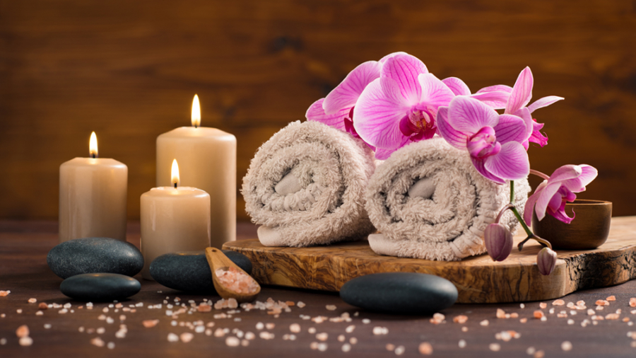 Spa setting with brown rolled towel, orchids and candles on wood. Relaxing spa concept with candles, towels and hot stones massage with himalayan pink salt. Beautiful composition for beauty treatment in a spa.