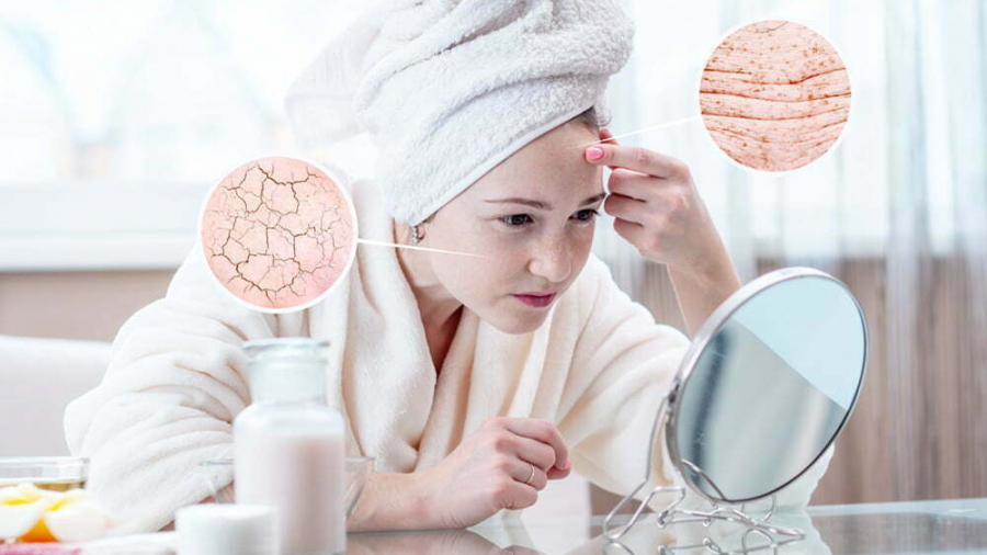 Beautiful young woman with a towel on her head looking at her dry skin with cracks and with first wrinkles. Circles increase the skin like a magnifying magnifier